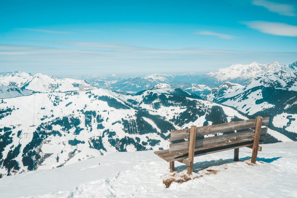 Holzbank mit Panoramablick über das schneebedeckte Skigebiet Saalbach Hinterglemm – Symbolfoto zu Skipasspreise Österreich.