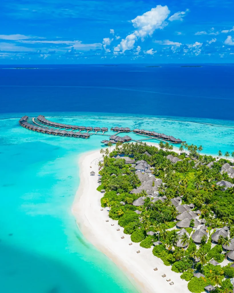 Luftaufnahme einer Malediven-Insel mit weißem Sandstrand, türkisfarbener Lagune und Overwater-Bungalows – beste Reisezeit Malediven
