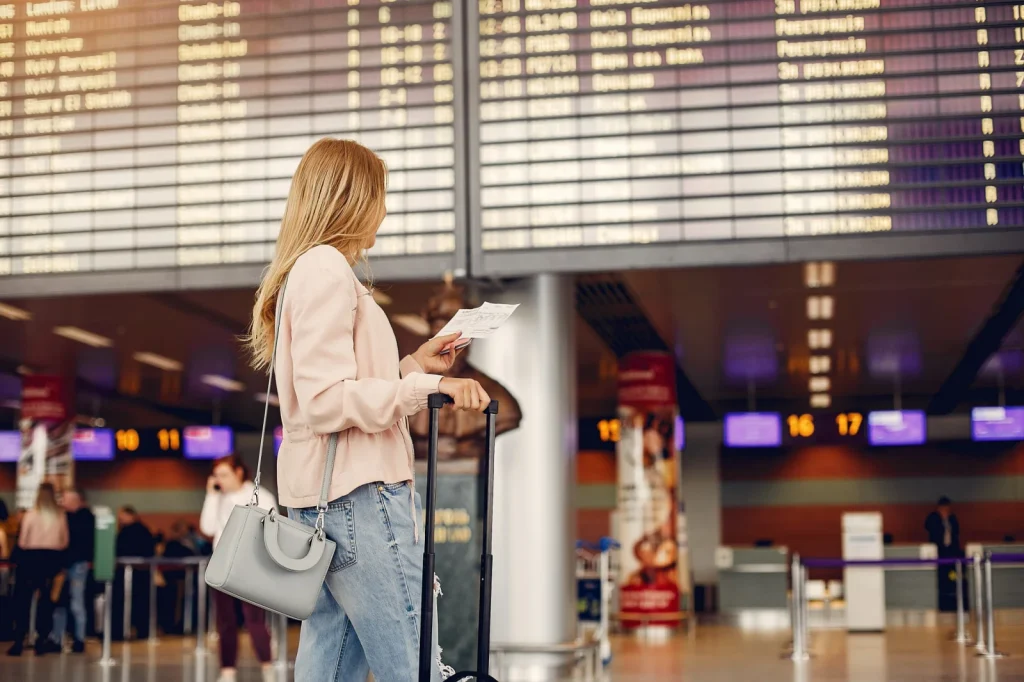 Reisende mit Trolley vor einer Abflugtafel am Flughafen